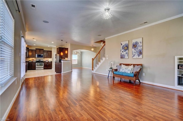 unfurnished living room featuring light wood-type flooring, arched walkways, visible vents, and a chandelier