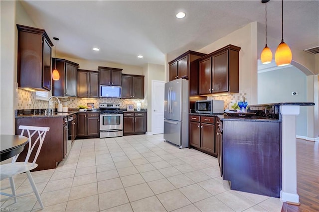 kitchen with pendant lighting, a sink, backsplash, dark brown cabinetry, and appliances with stainless steel finishes