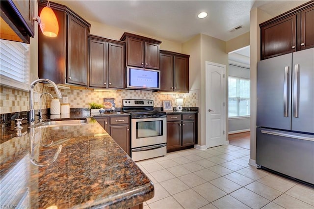 kitchen with visible vents, a sink, stainless steel appliances, light tile patterned floors, and decorative backsplash