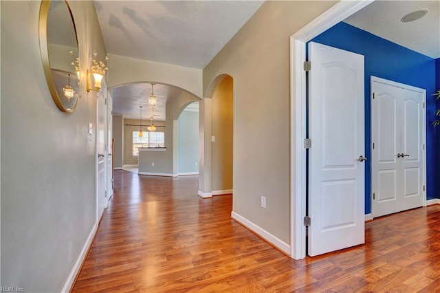 corridor with baseboards, arched walkways, a textured ceiling, and wood finished floors