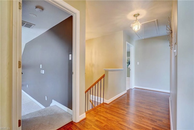 hallway with visible vents, an upstairs landing, wood finished floors, baseboards, and attic access