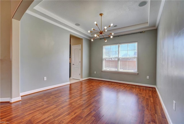 unfurnished room with a raised ceiling, wood finished floors, arched walkways, an inviting chandelier, and baseboards