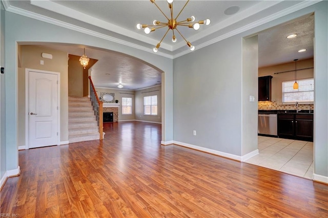 unfurnished living room with baseboards, a chandelier, light wood-style flooring, arched walkways, and a sink