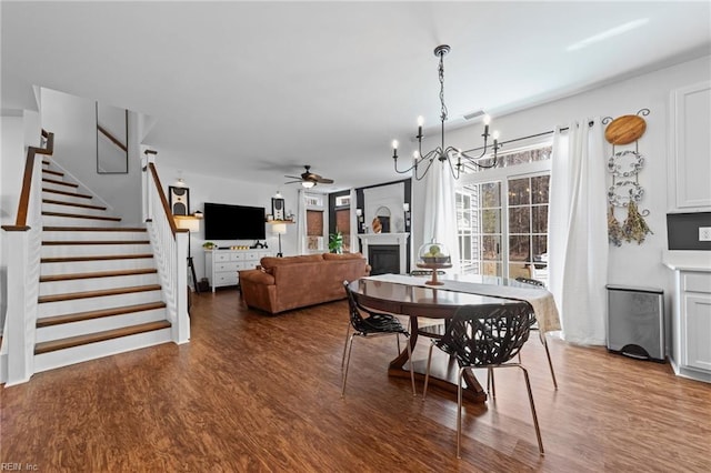 dining space featuring visible vents, ceiling fan with notable chandelier, wood finished floors, stairway, and a fireplace