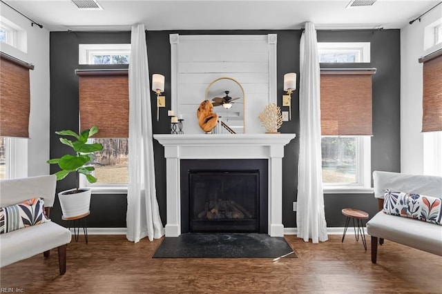 interior space featuring baseboards, a large fireplace, visible vents, and wood finished floors