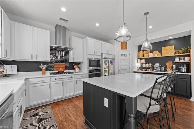 kitchen with visible vents, dark wood-type flooring, a kitchen island, wall chimney range hood, and built in appliances