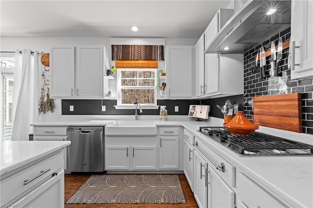 kitchen with a sink, backsplash, appliances with stainless steel finishes, wall chimney exhaust hood, and white cabinets