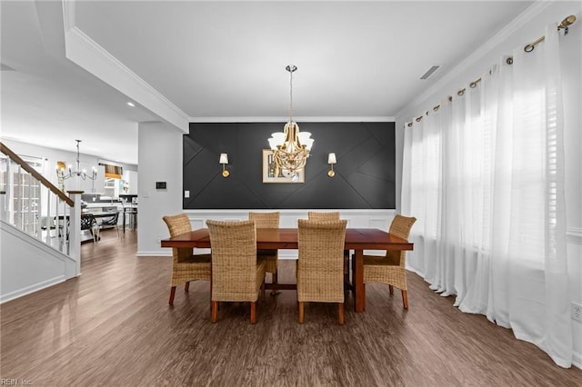 dining space with an accent wall, stairway, ornamental molding, wood finished floors, and a notable chandelier