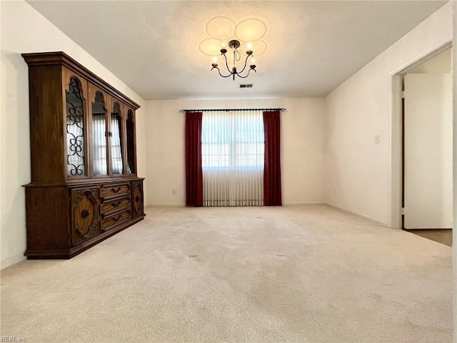 carpeted empty room featuring visible vents, a textured ceiling, and a chandelier