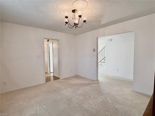 carpeted empty room with a textured ceiling, stairway, baseboards, and a chandelier