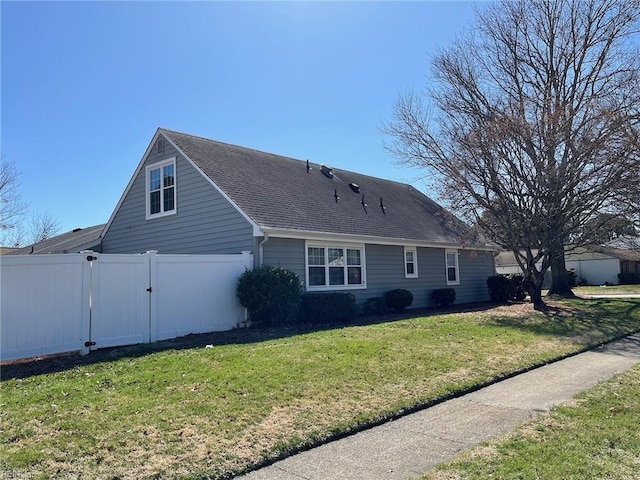 exterior space with a gate, a shingled roof, a yard, and fence