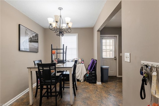 dining room featuring a chandelier, stone finish floor, and baseboards