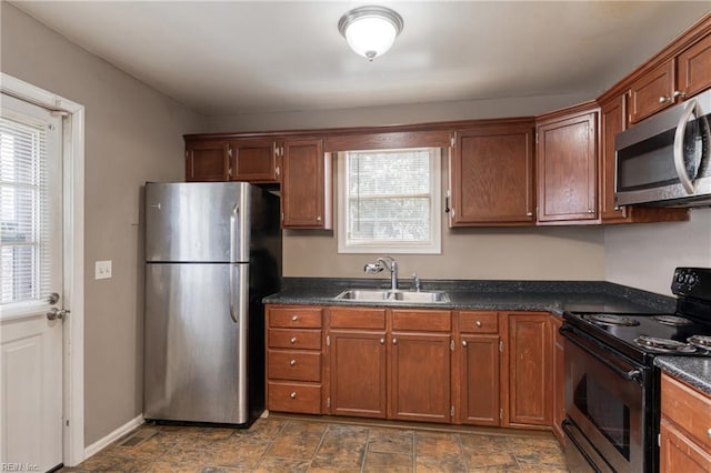 kitchen featuring dark countertops, baseboards, appliances with stainless steel finishes, brown cabinetry, and a sink