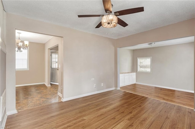 spare room with a textured ceiling, light wood-style floors, baseboards, and a healthy amount of sunlight