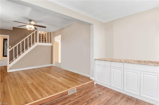 unfurnished room with visible vents, baseboards, light wood-style flooring, stairs, and a textured ceiling