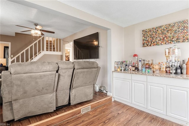 living room featuring visible vents, stairway, a dry bar, light wood-style flooring, and a ceiling fan