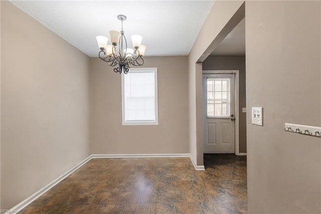 unfurnished dining area with an inviting chandelier, stone finish flooring, and baseboards