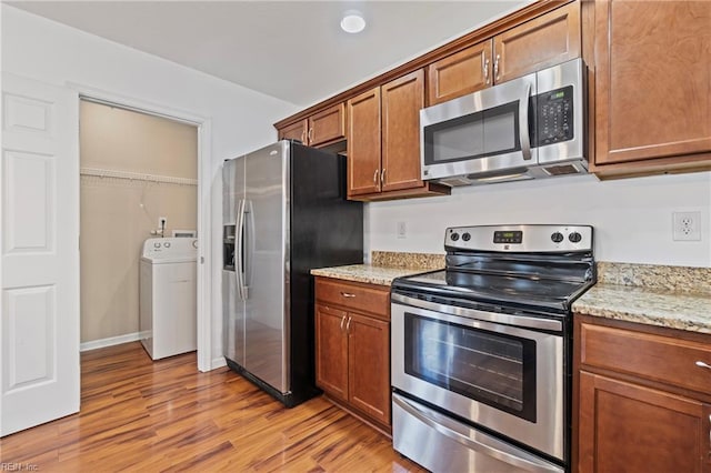 kitchen with stainless steel appliances, washer / clothes dryer, light wood-style flooring, and brown cabinetry