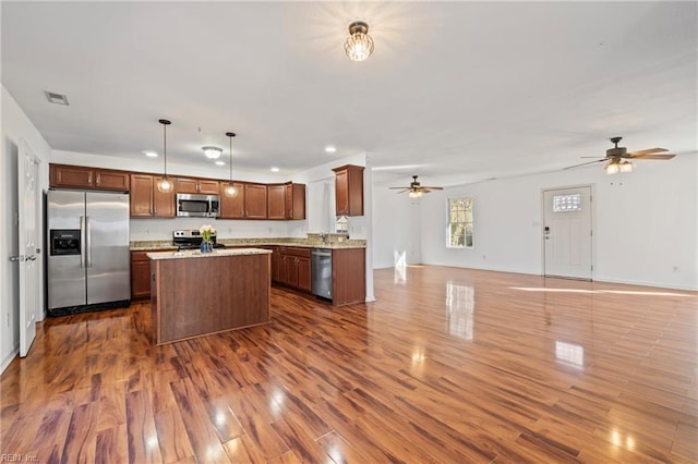 kitchen featuring dark wood-type flooring, pendant lighting, a kitchen island, open floor plan, and stainless steel appliances