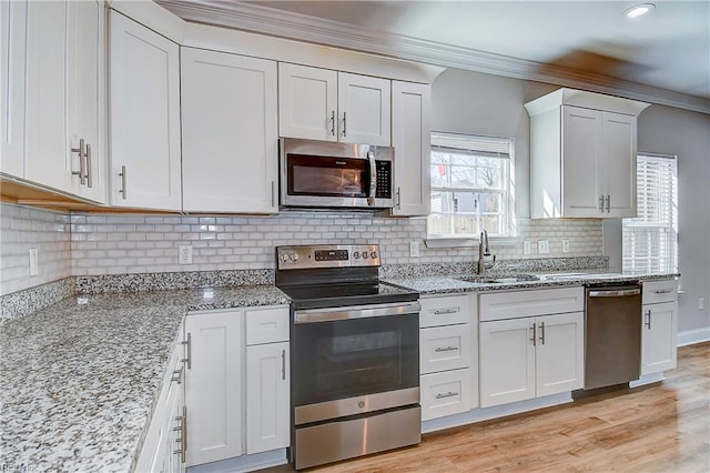 kitchen featuring a sink, light stone counters, white cabinetry, appliances with stainless steel finishes, and crown molding