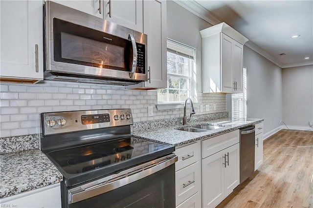 kitchen featuring ornamental molding, a sink, white cabinetry, stainless steel appliances, and light wood-style floors