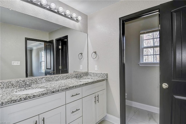 bathroom featuring double vanity, baseboards, a wealth of natural light, and a sink