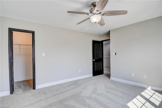 unfurnished bedroom with a walk in closet, visible vents, a closet, carpet floors, and baseboards