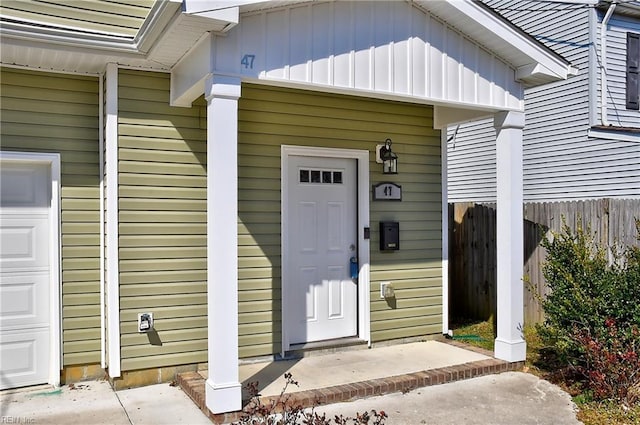 doorway to property with a garage, board and batten siding, and fence