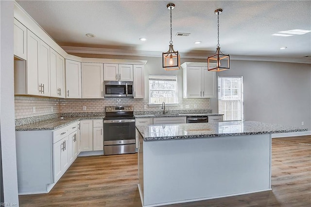 kitchen with wood finished floors, visible vents, a kitchen island, white cabinets, and appliances with stainless steel finishes