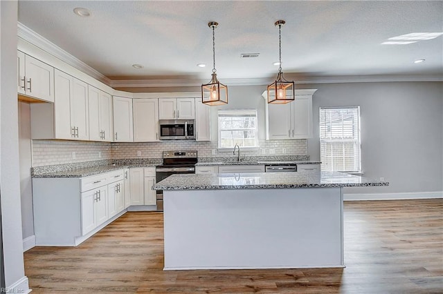 kitchen featuring light stone counters, visible vents, stainless steel appliances, white cabinetry, and a center island