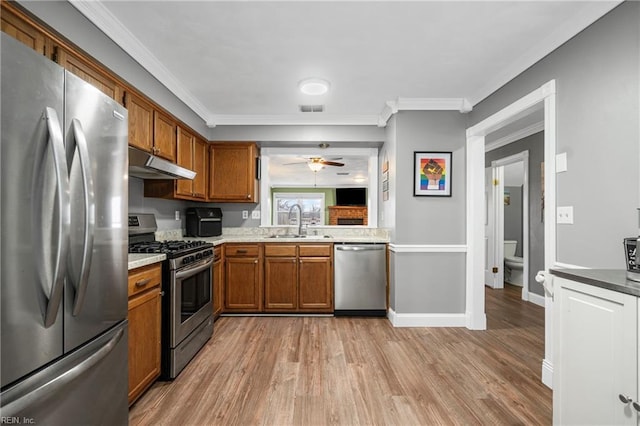 kitchen with brown cabinetry, visible vents, a sink, under cabinet range hood, and appliances with stainless steel finishes