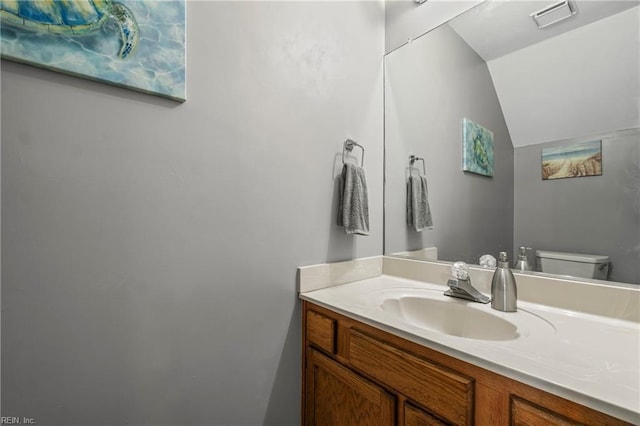 half bath with vanity, vaulted ceiling, toilet, and visible vents