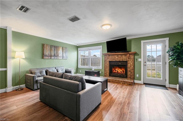 living area featuring visible vents, a brick fireplace, baseboards, and wood finished floors