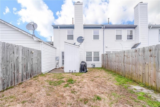 back of house featuring a lawn, a chimney, and a fenced backyard