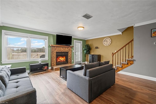 living room featuring visible vents, ornamental molding, wood finished floors, baseboards, and stairs