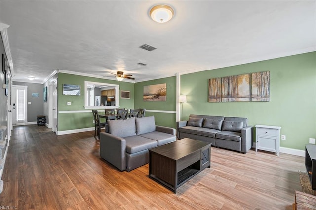 living area featuring visible vents, baseboards, wood finished floors, and ornamental molding