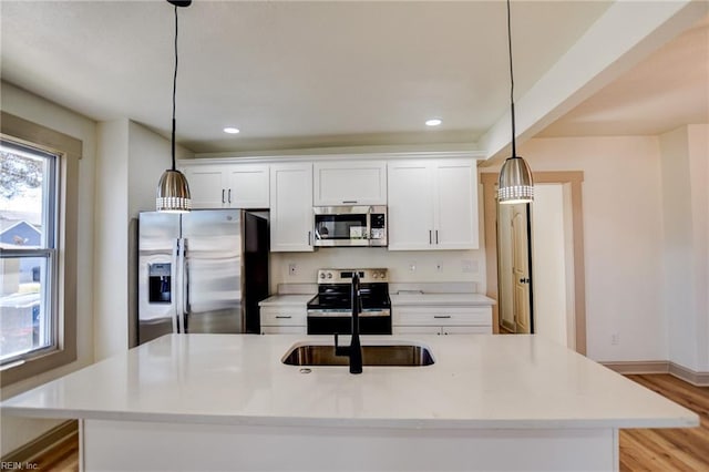 kitchen with hanging light fixtures, white cabinets, appliances with stainless steel finishes, and a sink