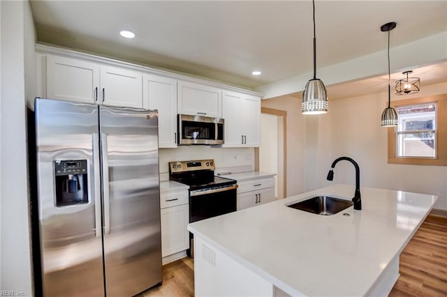 kitchen featuring light wood finished floors, a center island with sink, appliances with stainless steel finishes, white cabinetry, and a sink