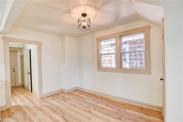 unfurnished room with lofted ceiling, light wood-type flooring, and baseboards