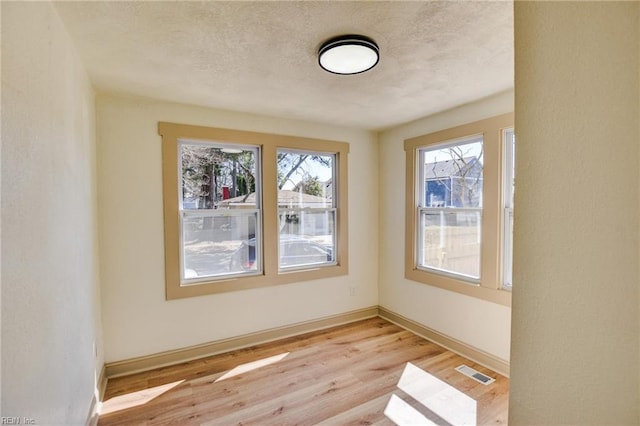 unfurnished room featuring light wood finished floors, visible vents, a textured ceiling, and baseboards