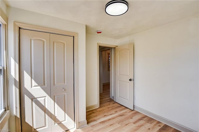 unfurnished bedroom featuring light wood-type flooring, baseboards, and a closet