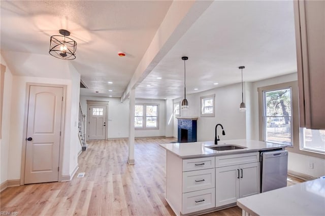 kitchen featuring light wood-style flooring, dishwasher, a fireplace, and a sink