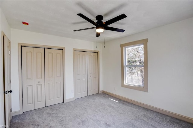 unfurnished bedroom with baseboards, two closets, carpet, and a ceiling fan