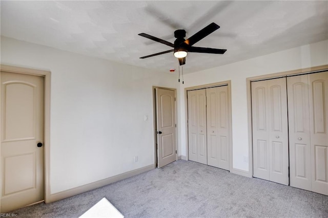 unfurnished bedroom with two closets, a ceiling fan, baseboards, and carpet floors