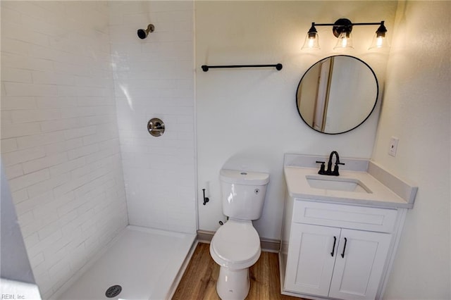 bathroom featuring toilet, wood finished floors, a tile shower, baseboards, and vanity