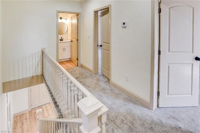 hall with a sink, baseboards, light colored carpet, and light wood finished floors