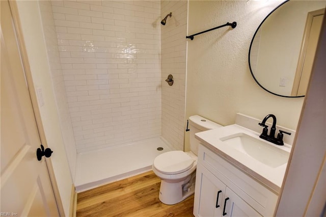 bathroom featuring toilet, wood finished floors, tiled shower, vanity, and a textured wall