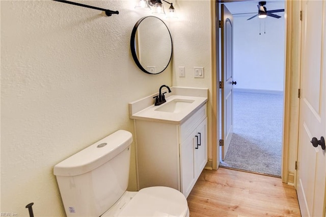 bathroom featuring toilet, a ceiling fan, wood finished floors, vanity, and a textured wall