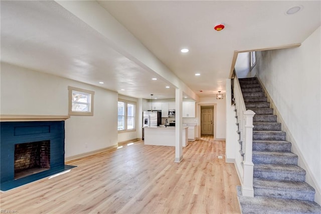 unfurnished living room featuring baseboards, stairway, light wood-type flooring, recessed lighting, and a fireplace