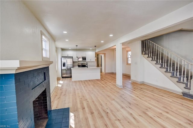 unfurnished living room with stairway, plenty of natural light, light wood-style floors, and a brick fireplace